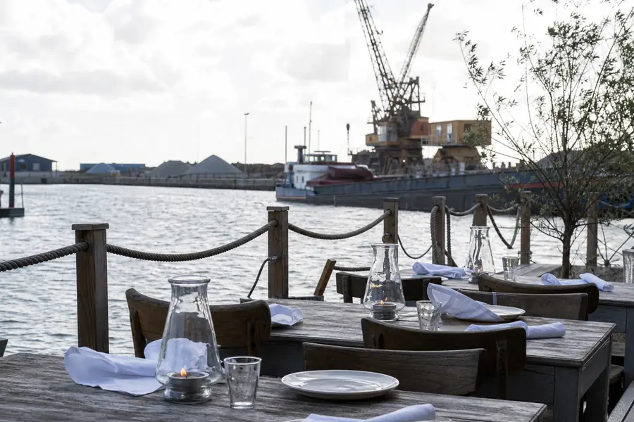 Terrasse am Wasser mit Holztischen und Blick auf Hafenkräne