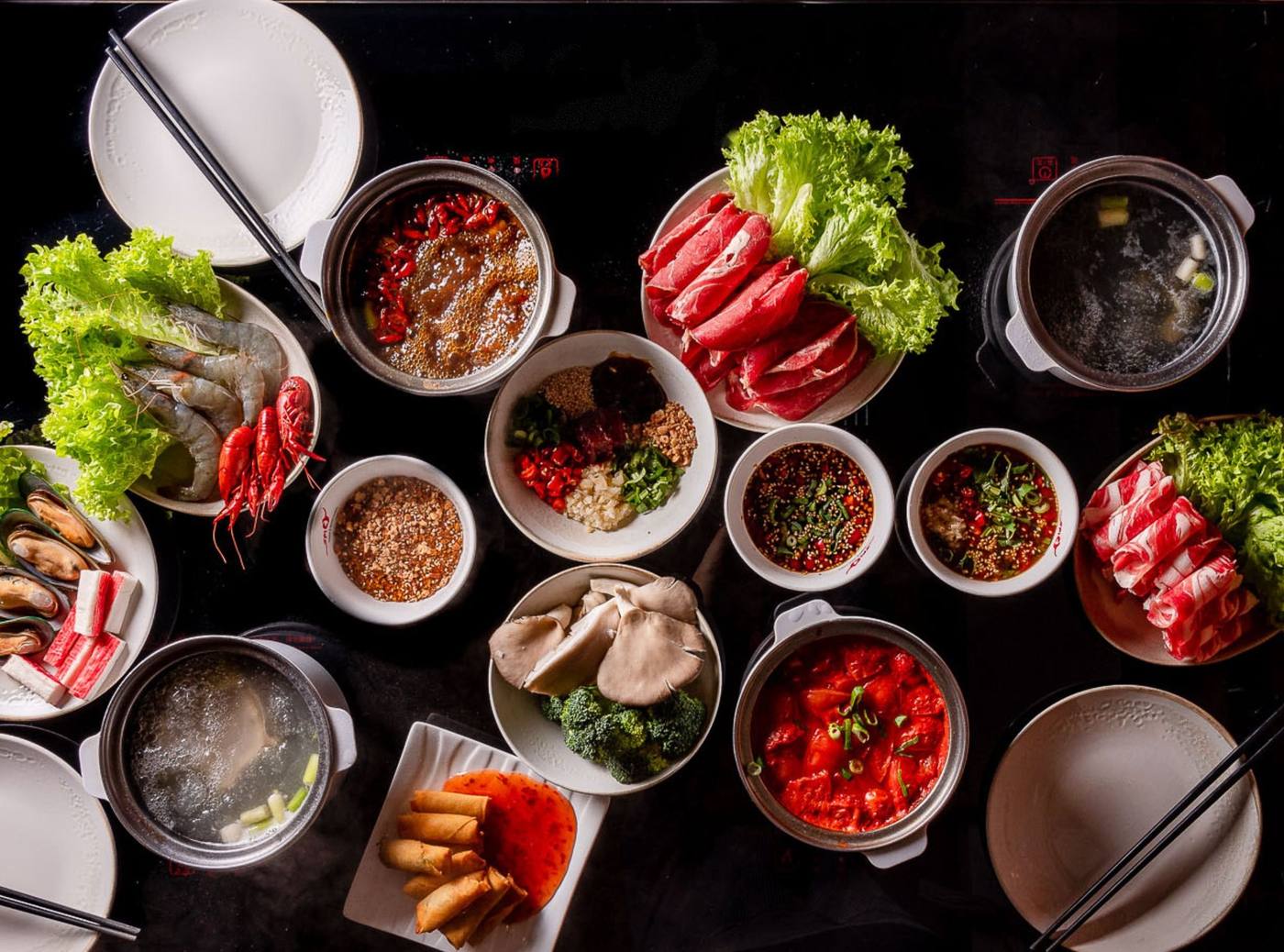 Gedeckter Hotpot-Tisch mit scharfer Brühe, Rindfleisch, Meeresfrüchten, Gemüse und selbst gemischten Dipsoßen