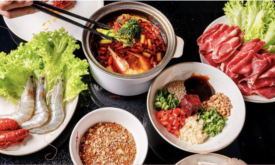 Hotpot-Tisch mit brodelnder scharfer Brühe, Garnelen, Rindfleisch und Dipsoßen